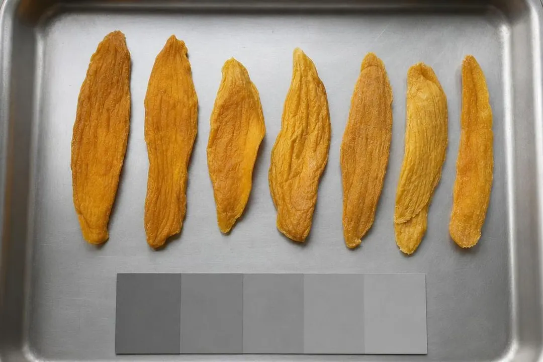 不锈钢检验托盘上排成一列的芒果干切片,旁边是一张纯灰色比色参考条