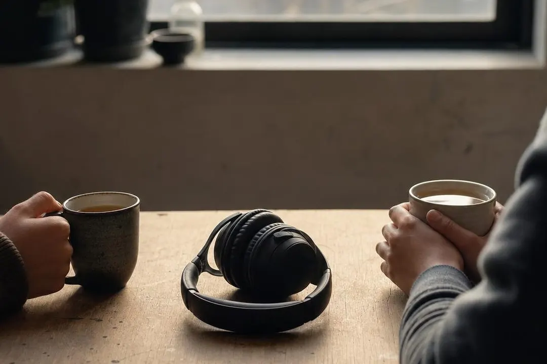 素色桌面上两杯茶与中间的头戴式耳机,午后窗光
